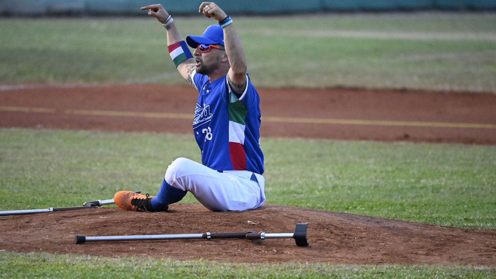 Un jugador italiano celebra sentado en el montículo, con sus muletas a un lado. Foto: WBSC.